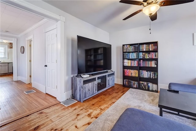 living room with crown molding, baseboards, visible vents, and light wood-type flooring