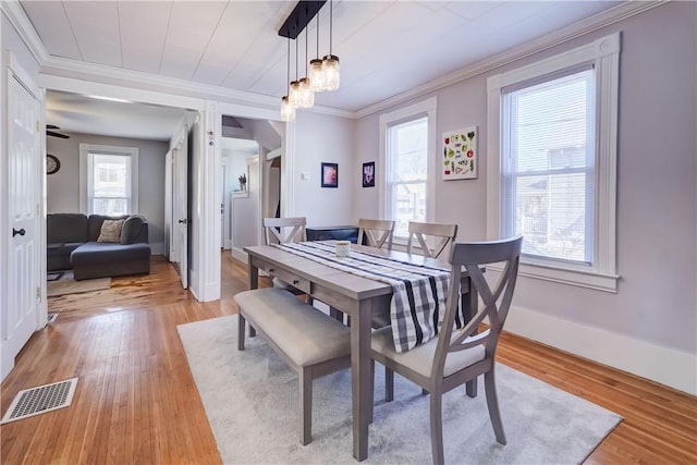 dining space with light wood-type flooring, visible vents, a healthy amount of sunlight, and ornamental molding