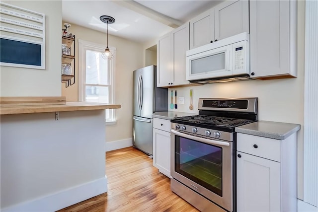 kitchen with white cabinets, appliances with stainless steel finishes, pendant lighting, and light wood-style flooring