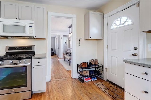 kitchen featuring light wood-style flooring, dark countertops, stainless steel range with gas cooktop, white cabinets, and white microwave