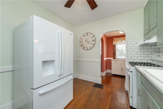 kitchen featuring white appliances, dark wood finished floors, light countertops, under cabinet range hood, and tasteful backsplash