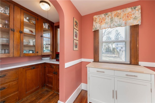 interior space featuring brown cabinets, dark wood-type flooring, arched walkways, white cabinets, and glass insert cabinets