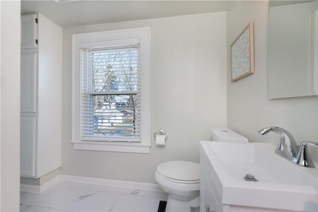 half bath featuring marble finish floor, toilet, vanity, and baseboards