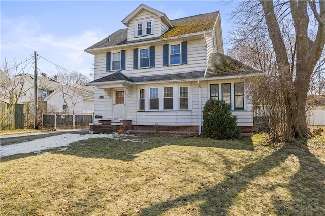 traditional style home with roof with shingles, a front yard, and fence