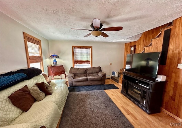 living area featuring light wood-type flooring, a textured ceiling, wood walls, and a baseboard radiator