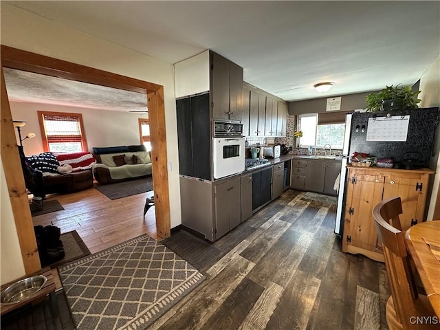 kitchen with dark wood finished floors, decorative backsplash, stainless steel gas cooktop, and oven