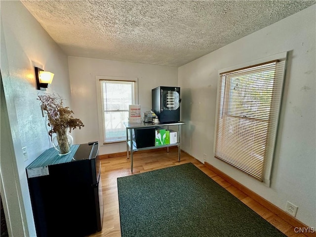 unfurnished office featuring baseboards, light wood-type flooring, and a textured ceiling