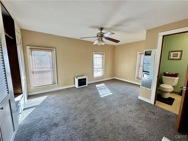 unfurnished bedroom featuring heating unit, baseboards, ceiling fan, dark carpet, and connected bathroom