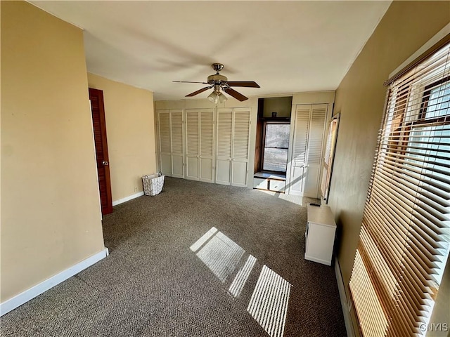 unfurnished bedroom featuring ceiling fan, baseboards, carpet floors, and multiple closets