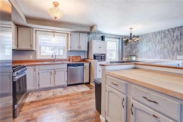 kitchen featuring light wood-type flooring, a notable chandelier, stainless steel appliances, wood counters, and a sink