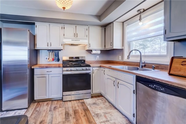 kitchen featuring light wood-style flooring, a sink, under cabinet range hood, appliances with stainless steel finishes, and wooden counters