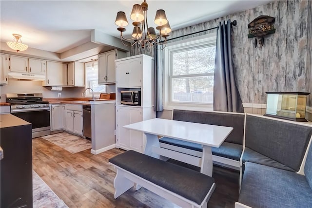 kitchen with light wood finished floors, a sink, under cabinet range hood, appliances with stainless steel finishes, and breakfast area