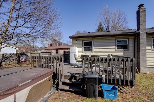 rear view of property with outdoor dining area, fence, a wooden deck, a chimney, and a hot tub