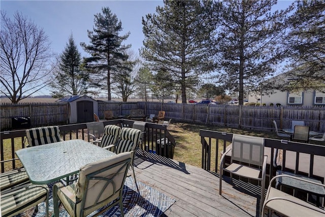 wooden terrace with a fenced backyard, outdoor dining space, a storage shed, and an outdoor structure