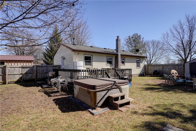 rear view of property featuring a yard, a fenced backyard, a chimney, a hot tub, and a deck