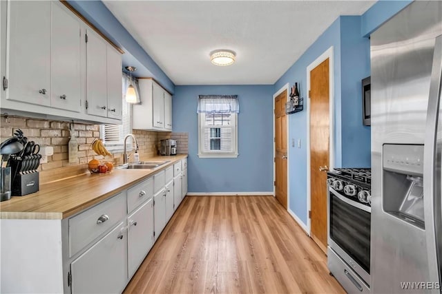 kitchen with backsplash, light countertops, appliances with stainless steel finishes, light wood-style floors, and a sink