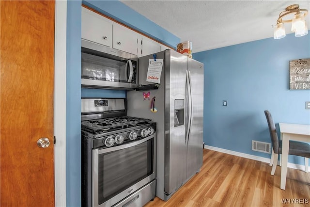 kitchen with visible vents, baseboards, light wood-style floors, white cabinets, and stainless steel appliances