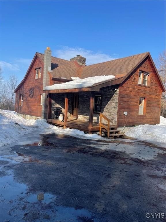 snow covered property with roof with shingles and a chimney