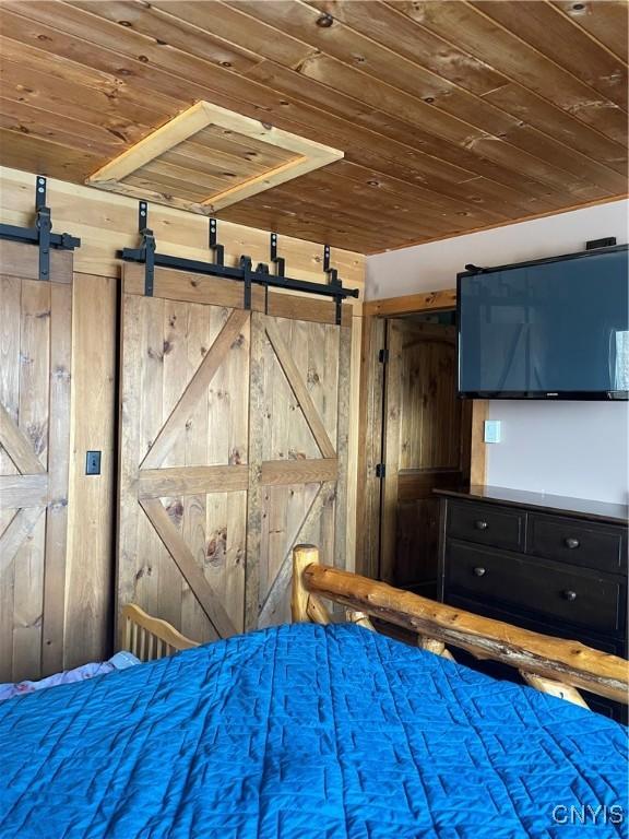 unfurnished bedroom with a barn door, wood walls, and wooden ceiling