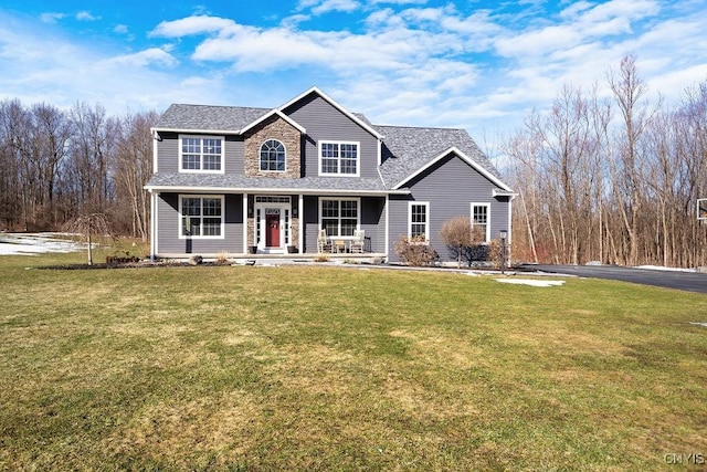 traditional home featuring a front yard, covered porch, stone siding, and a shingled roof