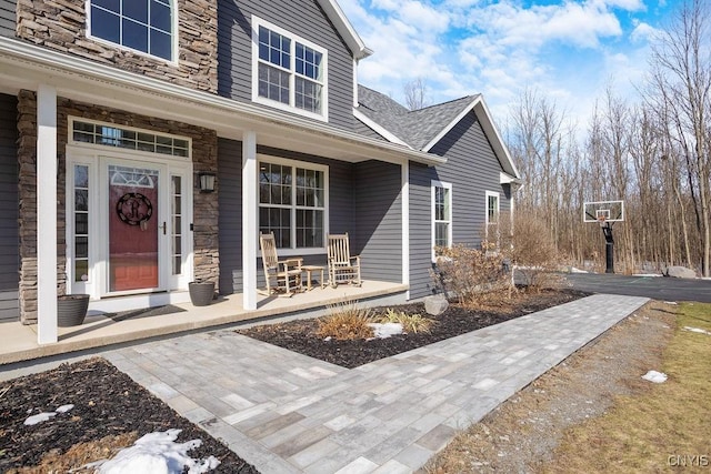 property entrance with covered porch, stone siding, and a shingled roof