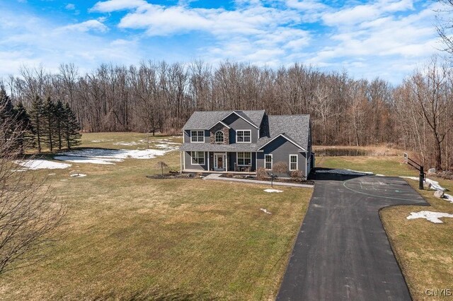 view of front of house with a wooded view, covered porch, driveway, and a front yard