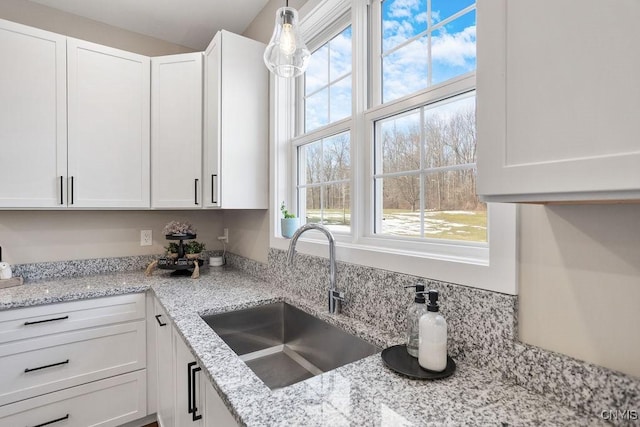 kitchen with white cabinets, light stone countertops, a wealth of natural light, and a sink