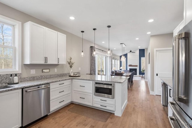 kitchen featuring a peninsula, white cabinets, light wood finished floors, and stainless steel appliances