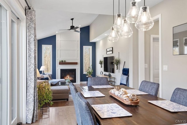 dining room featuring a ceiling fan, vaulted ceiling, wood finished floors, and a large fireplace