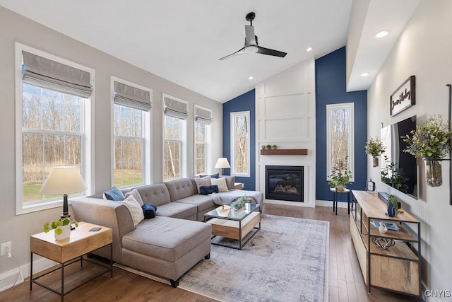 living area with wood finished floors, baseboards, high vaulted ceiling, ceiling fan, and a large fireplace