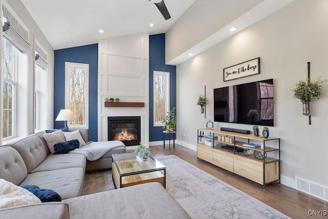 living room featuring visible vents, a large fireplace, baseboards, and wood finished floors