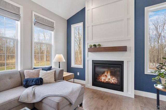 living area with a glass covered fireplace, vaulted ceiling, wood finished floors, and baseboards