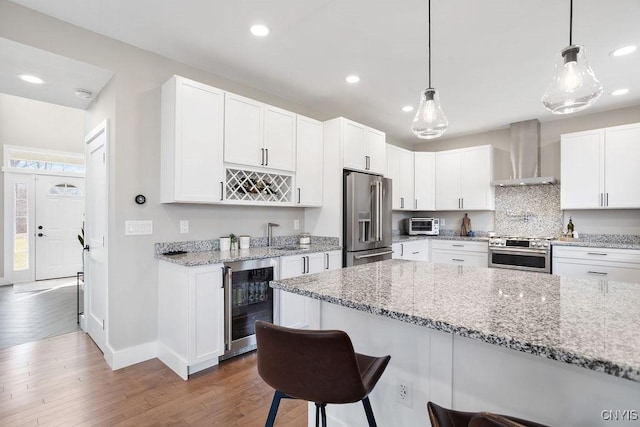 kitchen with a breakfast bar, wine cooler, white cabinets, appliances with stainless steel finishes, and wall chimney range hood