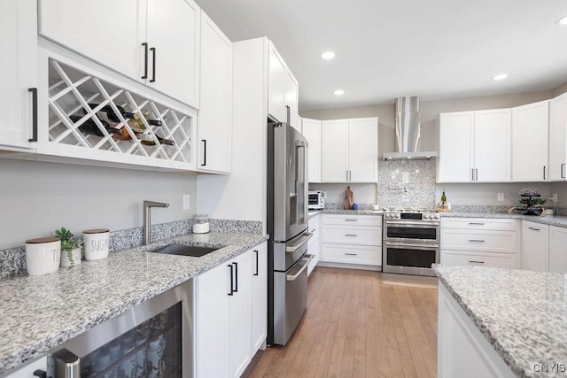 kitchen featuring beverage cooler, a sink, light wood-style floors, appliances with stainless steel finishes, and wall chimney exhaust hood