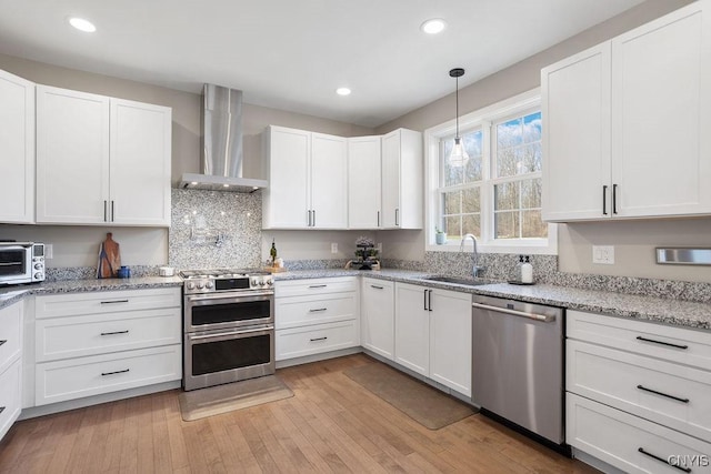 kitchen featuring a sink, stainless steel appliances, light wood-style flooring, and wall chimney range hood