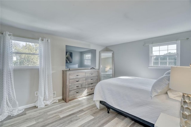 bedroom featuring multiple windows, light wood-style floors, and baseboards