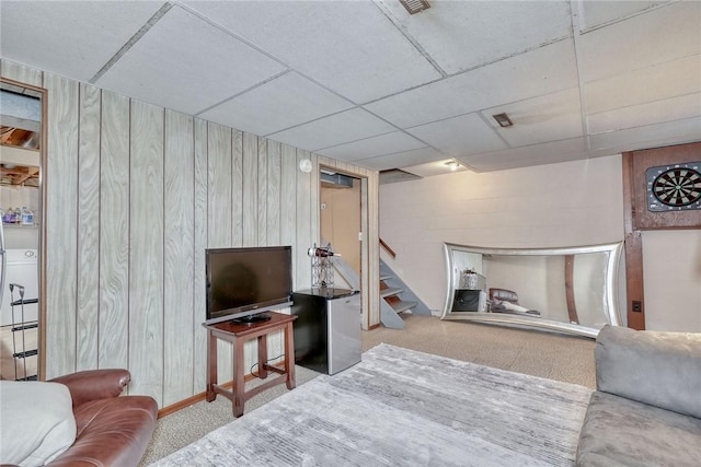 living area with stairway, wooden walls, and a drop ceiling