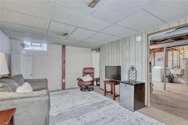 living room with a drop ceiling, washer / clothes dryer, wooden walls, and visible vents