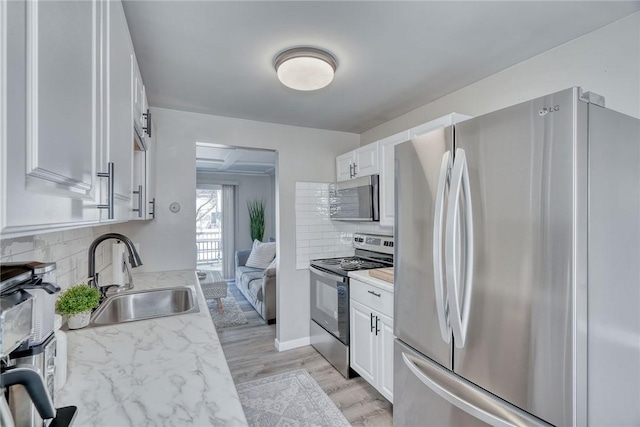 kitchen with a sink, light countertops, appliances with stainless steel finishes, white cabinetry, and light wood-type flooring