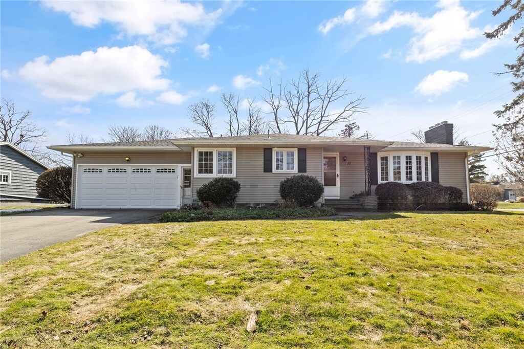 ranch-style home featuring a front lawn, an attached garage, a chimney, and driveway
