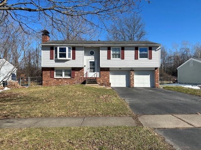 raised ranch featuring brick siding, a front lawn, aphalt driveway, a chimney, and an attached garage