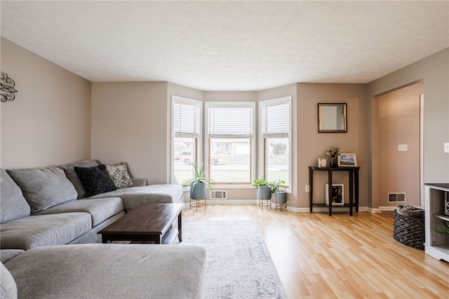 living area featuring light wood-type flooring, baseboards, a textured ceiling, and visible vents