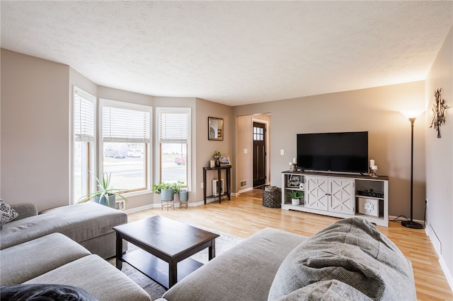 living room with a textured ceiling, light wood-type flooring, and baseboards