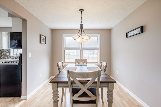 dining space with light wood-style flooring, baseboards, and a textured ceiling