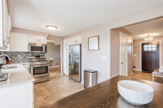 kitchen featuring light stone counters, a sink, decorative backsplash, stainless steel appliances, and white cabinetry