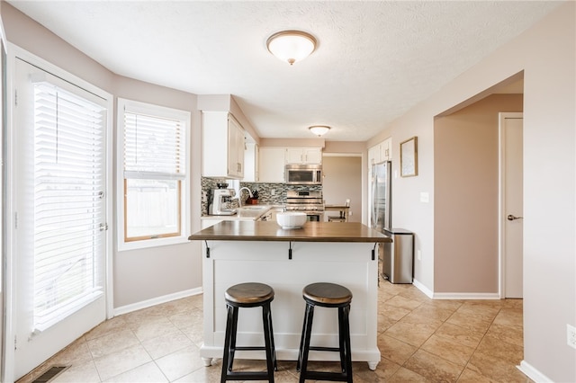 kitchen featuring a sink, stainless steel appliances, white cabinets, dark countertops, and tasteful backsplash