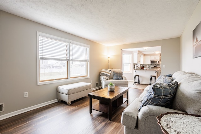 living area featuring visible vents, wood finished floors, baseboards, and a textured ceiling