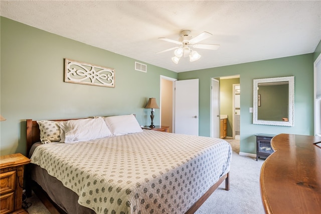 bedroom with a ceiling fan, light colored carpet, visible vents, and connected bathroom