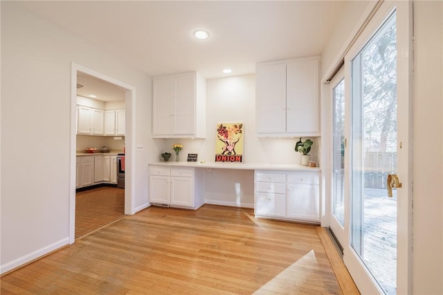 kitchen with light wood-type flooring, electric stove, built in desk, white cabinets, and light countertops