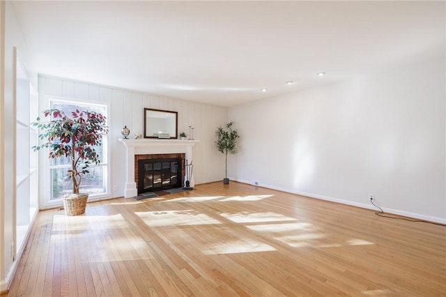 unfurnished living room with light wood finished floors, a brick fireplace, and baseboards